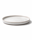 Side view of handmade white ceramic dinner plate with beige rim, shallow profile and subtle wheel-thrown texture