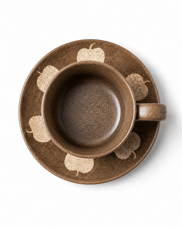 Top view of brown apple pattern ceramic cup and matching saucer on white background