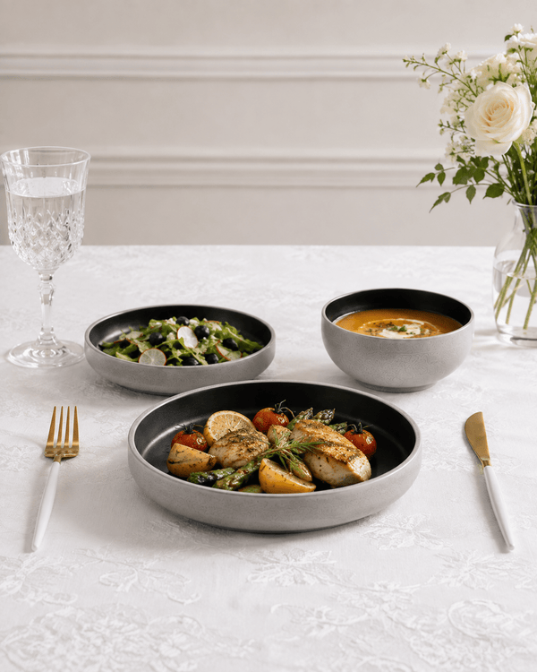 Handmade black and grey ceramic dinnerware set styled with food on a white European tablecloth