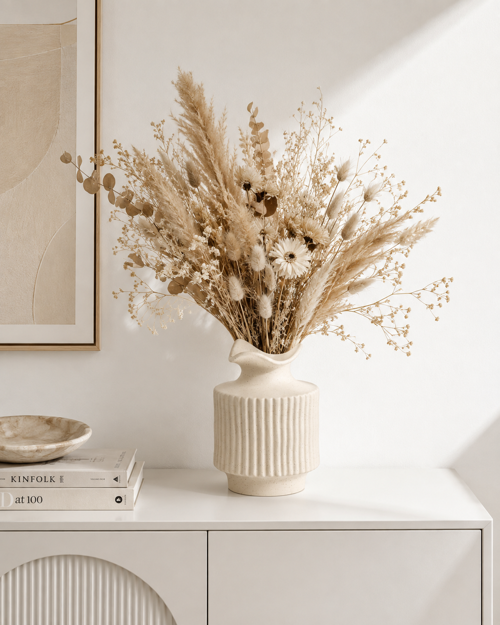 Handmade off-white ribbed ceramic vase styled with dried flowers on a white living room sideboard