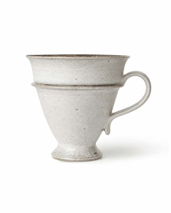 Side view of handmade speckled stoneware footed coffee mug with flared rim, pedestal base and curved handle