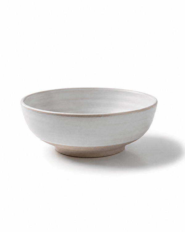 Side view of handmade white ceramic serving bowl with beige foot ring, softly rounded profile and natural glazed finish