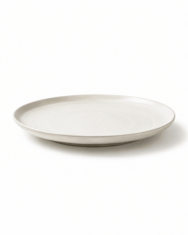 Side view of handmade white speckled ceramic dinner plate with shallow profile and raised rim