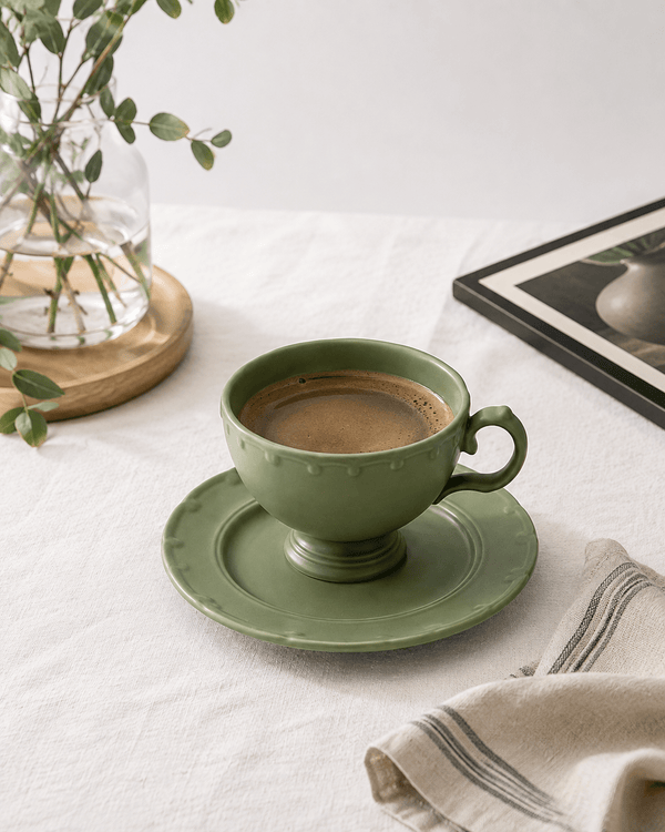 Olive green ceramic coffee cup and saucer with fresh coffee styled on a neutral table setting