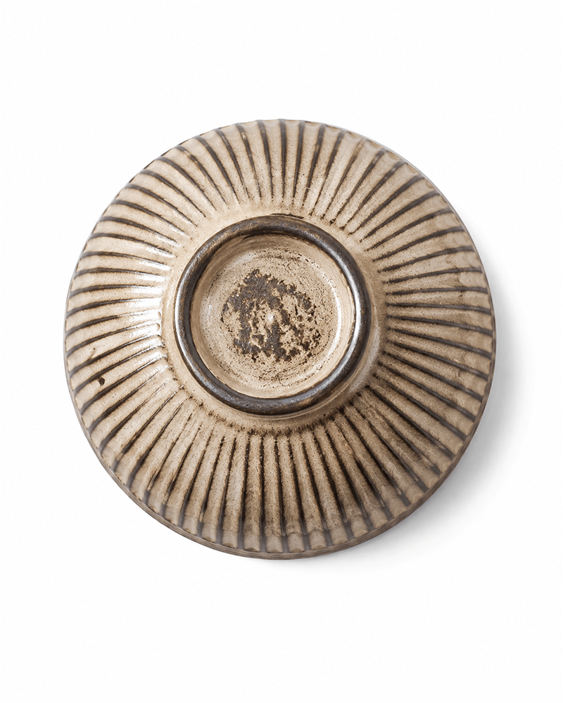 Bottom view of a fluted beige ceramic bowl highlighting natural foot ring and detailed ribbed stoneware texture