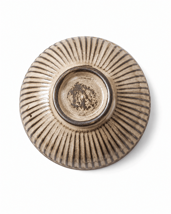 Bottom view of a fluted beige ceramic bowl highlighting natural foot ring and detailed ribbed stoneware texture