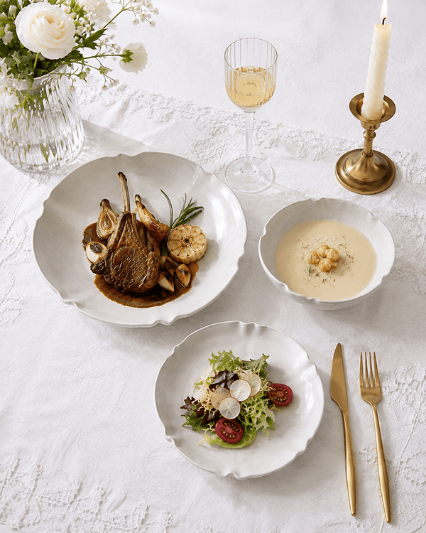 White scalloped ceramic dinnerware with plated food on an elegant white table setting